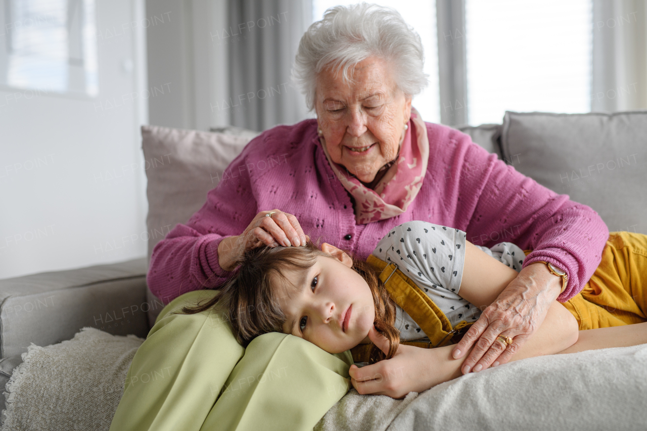 Sad girl lying head on gradmother knees and crying, grandma soothing her, caressing her hair. Portrait of an elderly woman spending time with granddaughter.