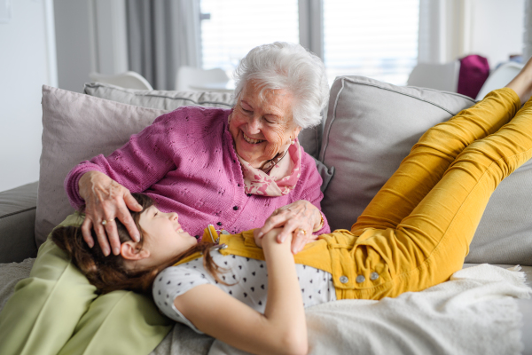 Cute girl lying head on gradmother knees, caressing her hair. Portrait of an elderly woman spending time with granddaughter.