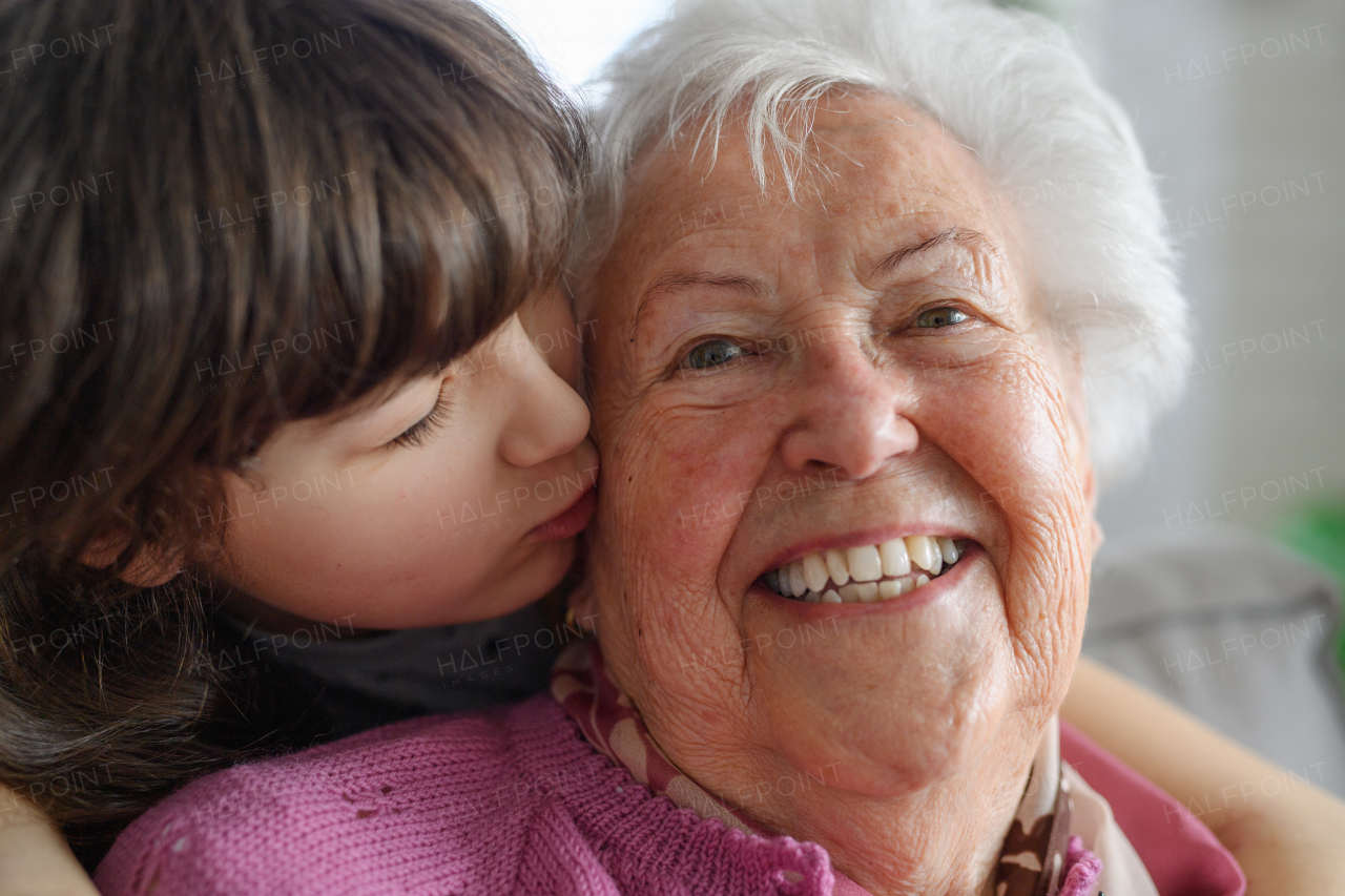 Cute girl hugging and kissing gradmother on her cheek from behind. Portrait of an elderly woman spending time with granddaughter.