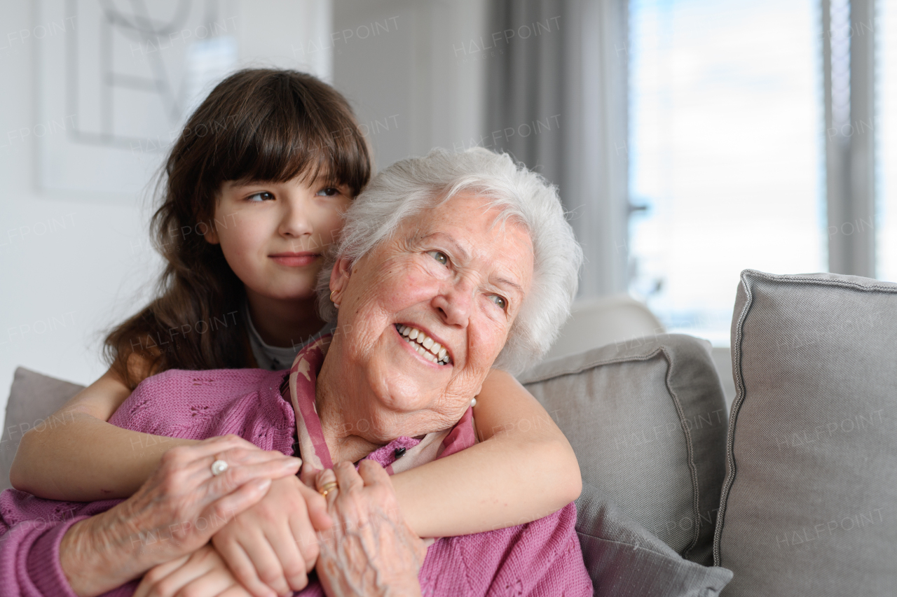 Cute girl hugging gradmother from behind, smiling. Portrait of an elderly woman spending time with granddaughter.