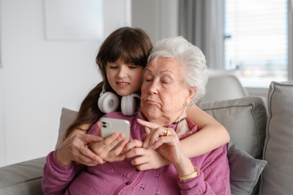 Grandmother with cute girl scrolling on smartphone, girl teaching senior woman to work with technology, internet. Portrait of an elderly woman spending time with granddaughter.