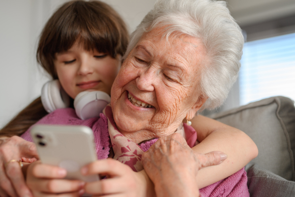 Grandmother with cute girl scrolling on smartphone, girl teaching senior woman to work with technology, internet. Portrait of an elderly woman spending time with granddaughter.