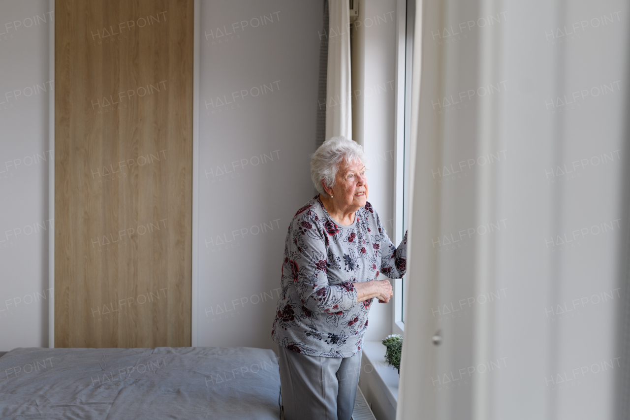 Senior woman looking out of window, spending time alone in apartment. Concept of loneliness and dependence of retired people.