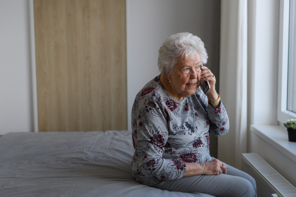 Senior woman making phone call spending time alone in apartment. Concept of loneliness and dependence of retired people.