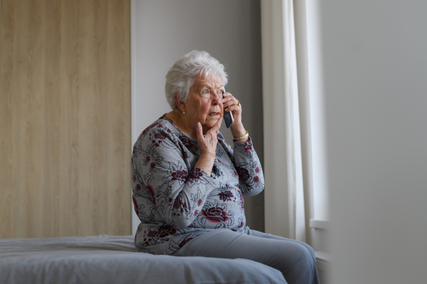 Senior woman making phone call spending time alone in apartment. Concept of loneliness and dependence of retired people.