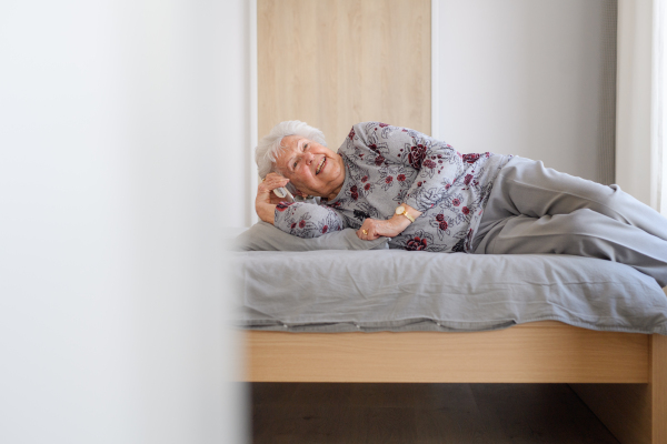 Senior woman lying in bed, phone calling on smartphone and smiling. Older woman using modern technology, digital skill and literacy.