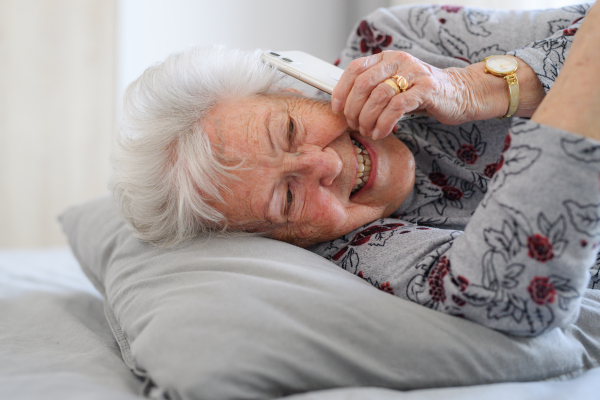 Senior woman lying in bed, phone calling on smartphone and smiling. Older woman using modern technology, digital skill and literacy.