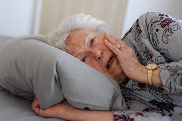 Senior woman lying in bed alone. Woman having pain a feeling anxious. Loneliness and social isolation of eldery woman.