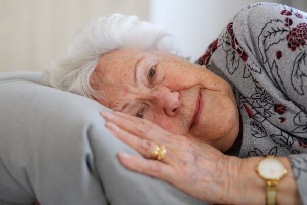 Senior woman lying in her bed alone, feeling anxious. Loneliness and social isolation of eldery woman.