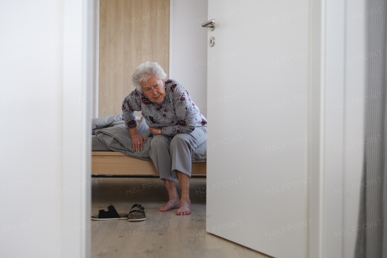 Senior woman trying to stand up from bed, feeling pain, holding abdomen.