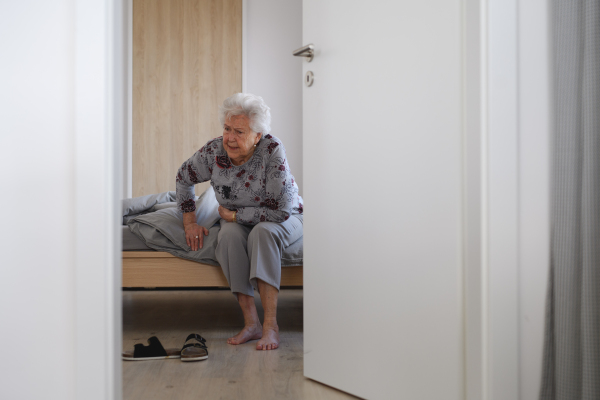 Senior woman trying to stand up from bed, feeling pain, holding abdomen.