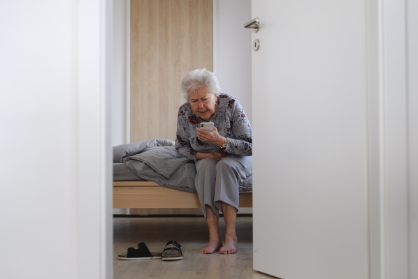 Senior woman trying to stand up from bed, feeling pain, holding abdomen.