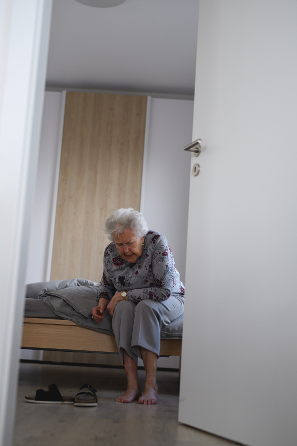 Senior woman trying to stand up from bed, feeling pain, holding abdomen.