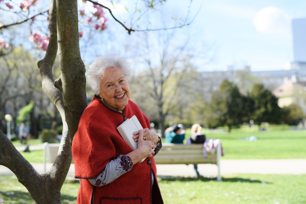 Elderly woman reading book outdoor, in park, having relaxing moment. Grandmother reading the bible in the cemetery.