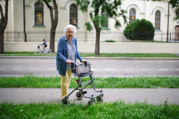 Beautiful elderly woman walking on city street with rollator, going grocery shopping to the store.