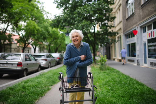 Beautiful elderly woman walking on city street with rollator, going grocery shopping to the store. Feeling cold.