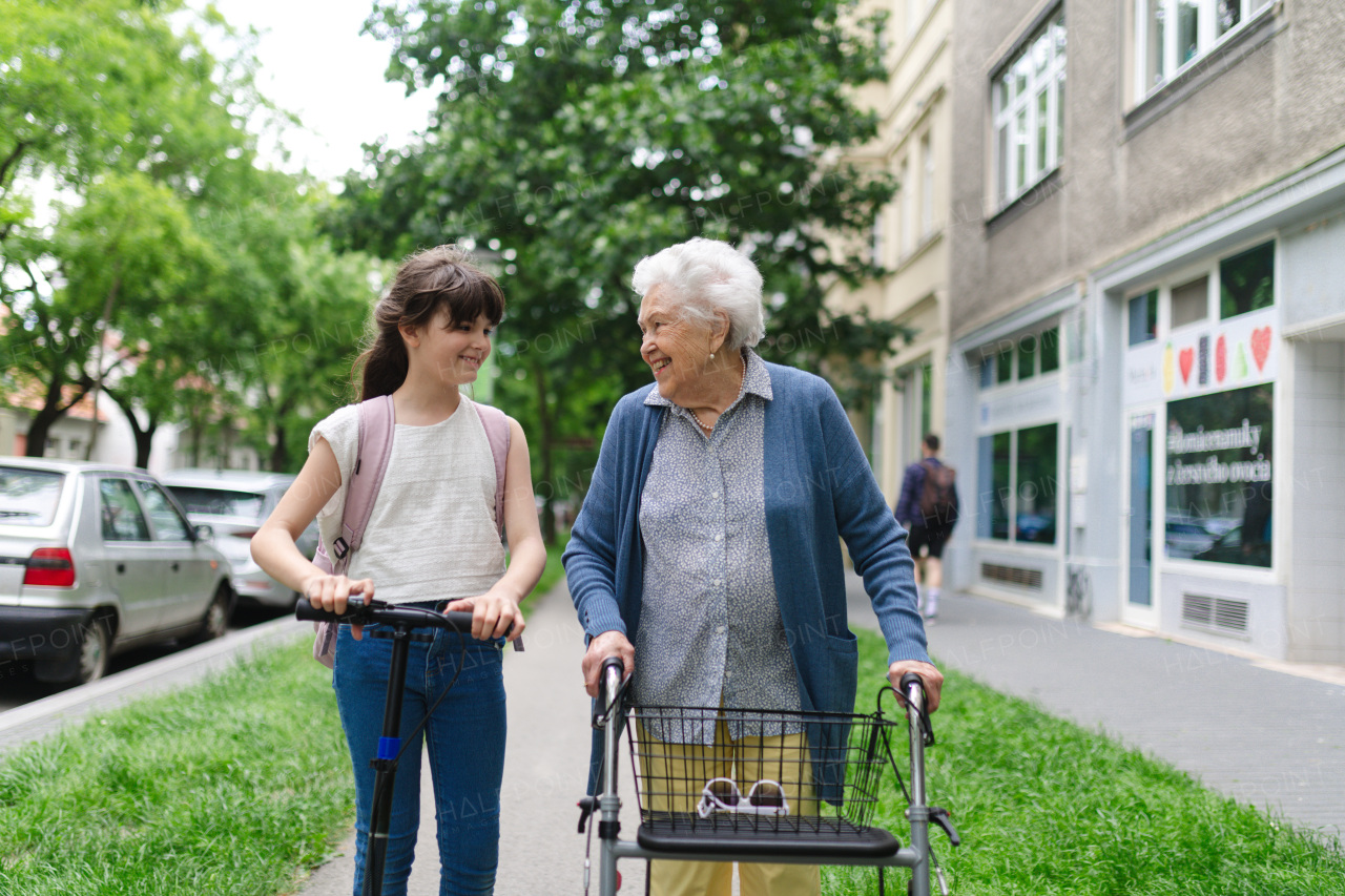 Grandma with walker picking up a young girl from school in the afternoon. Granddaughter spending time with her senior grandmother outdoors in the city after school.