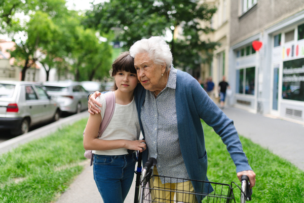 Grandma with walker picking up a young girl from school in the afternoon. Granddaughter spending time with her senior grandmother outdoors in the city after school.