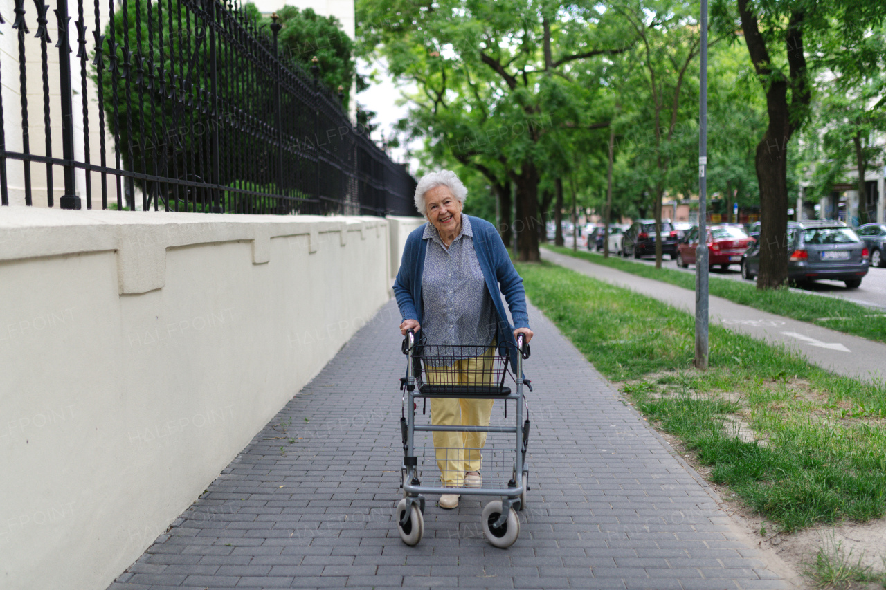 Beautiful elderly woman walking on city street with rollator, going grocery shopping to the store.