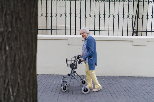 Beautiful elderly woman walking on city street with rollator, going grocery shopping to the store.