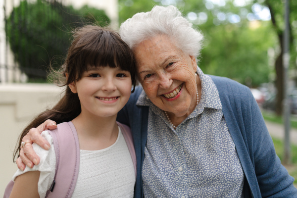 Grandma picking up a young girl from school in the afternoon. Granddaughter spending time with her senior grandmother outdoors in the city after school.