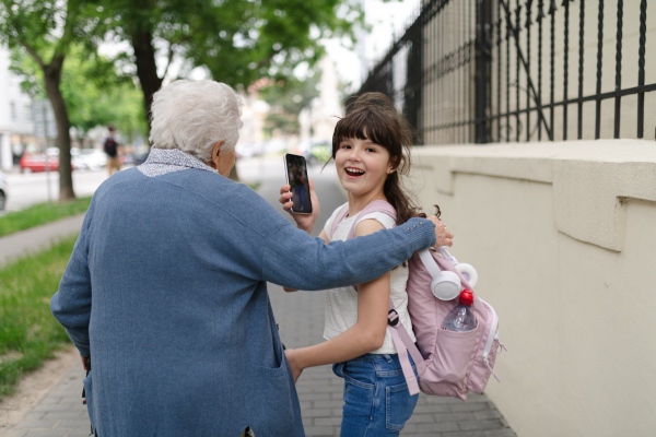 Grandma picking up girl after first day of school. Granddaughter spending time with her senior grandmother outdoors in the city.