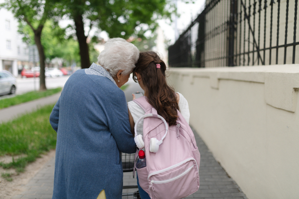 Grandma picking up girl after first day of school. Granddaughter spending time with her senior grandmother outdoors in the city, walking.