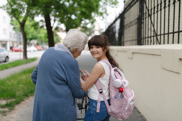 Grandma picking up girl after first day of school. Granddaughter spending time with her senior grandmother outdoors in the city, walking.