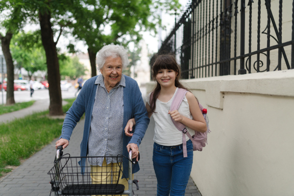 Grandma picking up girl after first day of school. Granddaughter spending time with her senior grandmother outdoors in the city, walking.