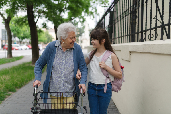 Grandma picking up girl after first day of school. Granddaughter spending time with her senior grandmother outdoors in the city, walking.