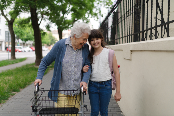 Grandma picking up girl after first day of school. Granddaughter spending time with her senior grandmother outdoors in the city, walking.