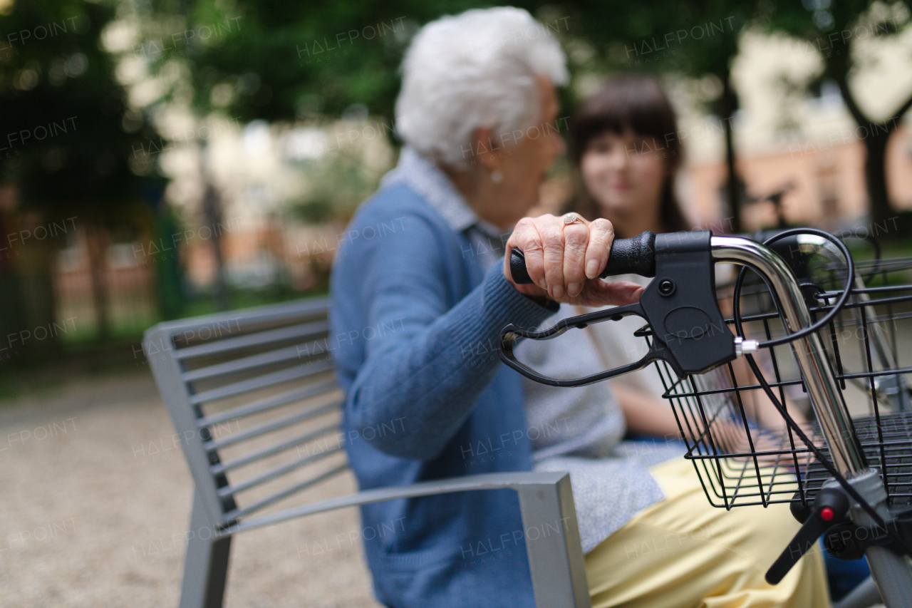 Grandma with walker spending time with granddaughter in city park, sitting on bench at children playground, talking.