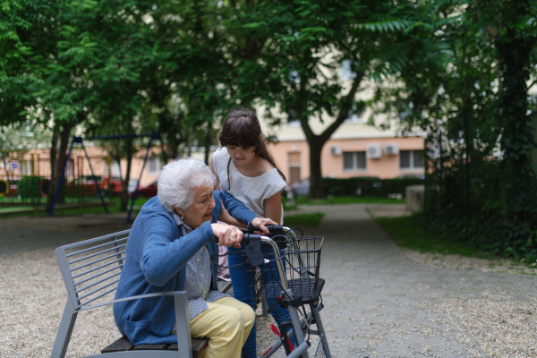 Girl helping gradma with walker to stand up from bench