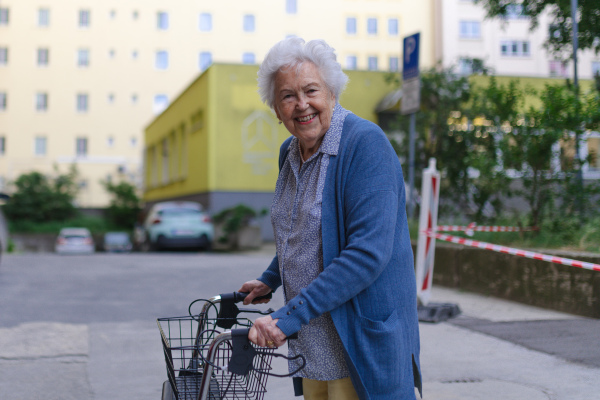 Beautiful elderly woman walking on city street with rollator, going grocery shopping to the store.