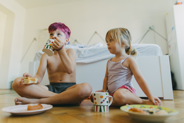 Siblings sitting on the floor and having a snack in their children's room. Young boy and girl watching television while eating. Bundt cake and hot cocoa for breakfast during the holidays.