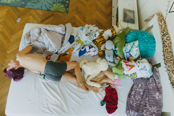 Top view of siblings lying on the bed and watching television. The children spending time indoors while raining during summer break. Longer screen time during holidays.