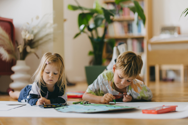 Siblings lying on stomach, painting at home with watercolors, markers and tempera paints, creating a model of planet Earth. A creative project at home during the holidays. A young student preparing a school project on the topic of planet conservation, climate change and Earth day.