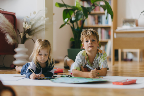 Siblings lying on stomach, painting at home with watercolors, markers and tempera paints, creating a model of planet Earth. A creative project at home during the holidays. A young student preparing a school project on the topic of planet conservation, climate change and Earth day.