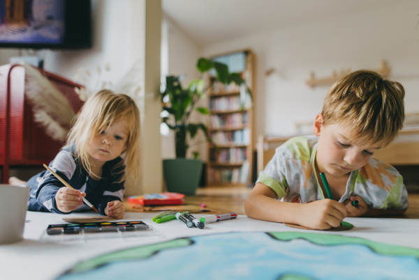 Siblings lying on stomach, painting at home with watercolors, markers and tempera paints, creating a model of planet Earth. A creative project at home during the holidays. A young student preparing a school project on the topic of planet conservation, climate change and Earth day.