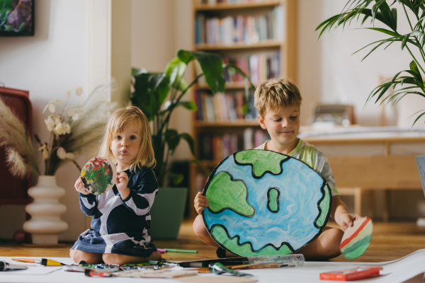 Siblings painting at home with watercolors and tempera paints, creating a model of planet Earth. A creative project at home during the holidays. A young student preparing a school project on the topic of planet conservation, climate change and Earth day.