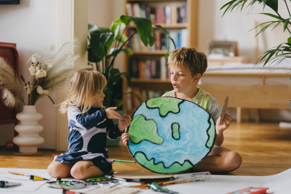 Siblings painting at home with watercolors and tempera paints, creating a model of planet Earth. A creative project at home during the holidays. A young student preparing a school project on the topic of planet conservation, climate change and Earth day.