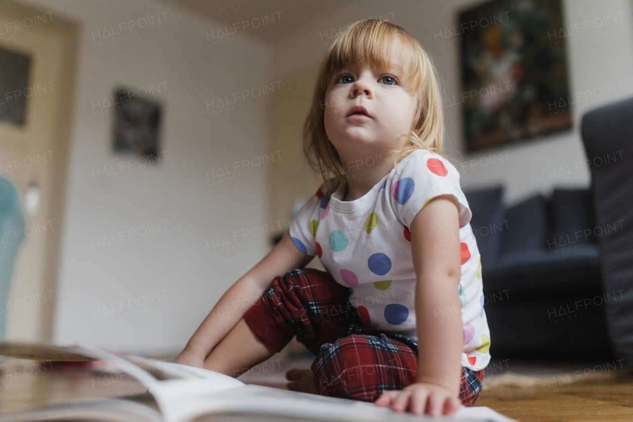 Cute little girl with bangs reading book sitting on the floor in her child's room.