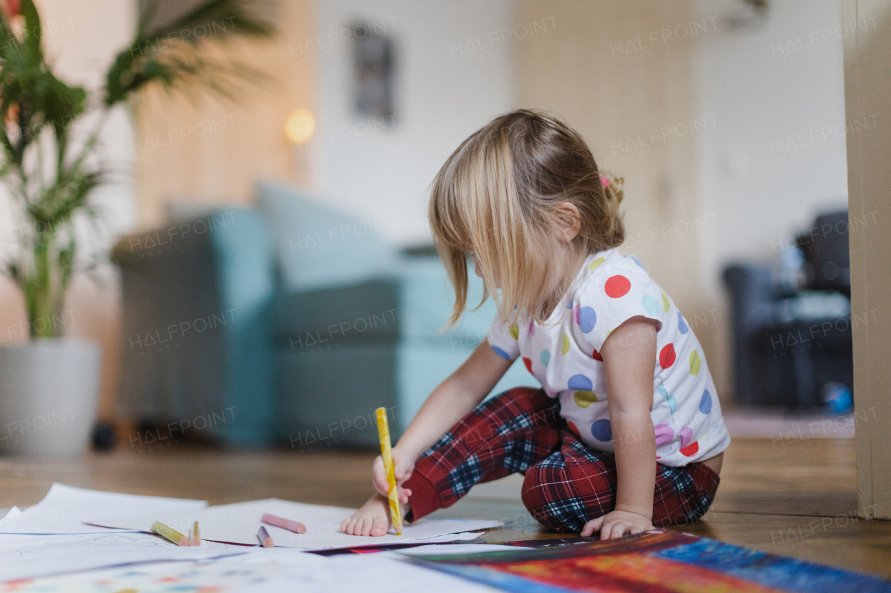 Cute little girl drawing with crayons, sitting on the floor in the living room. Outlining her own foot on paper.