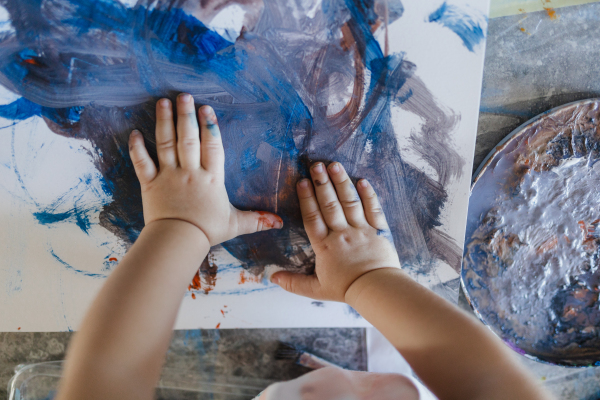 Cute little girl painting with her own hands, using tempera paint. Finger painting creative activity.