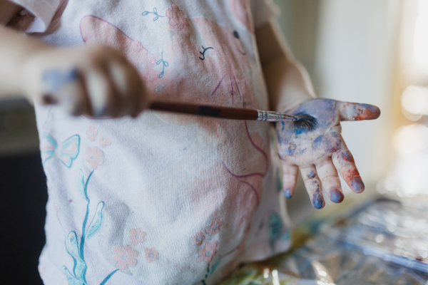 Close up of little girl painting on her own hand with tempera paint, using a paintbrush.