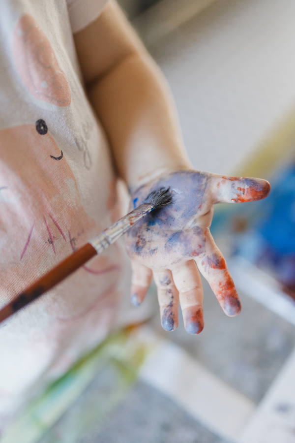 Close up of little girl painting on her own hand with tempera paint, using a paintbrush.