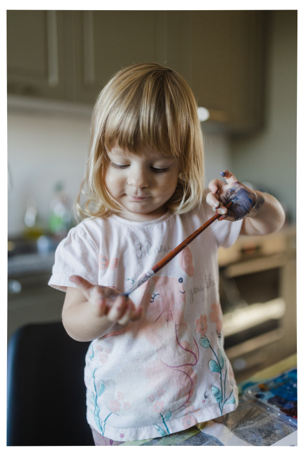 Cute little girl painting on her own hand with tempera paint, using a paintbrush.