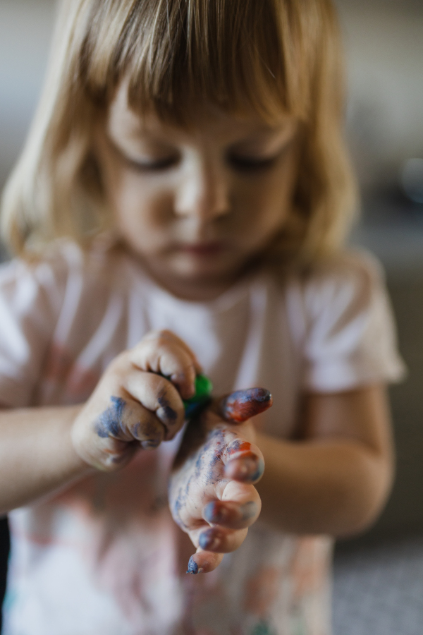 Portrait of little girl with messy hands stained with paint. Artistic kid getting messy and having fun.