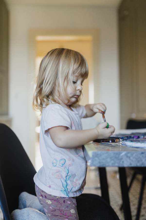 Cute little girl painting with tempera paint at home, using a paintbrush.