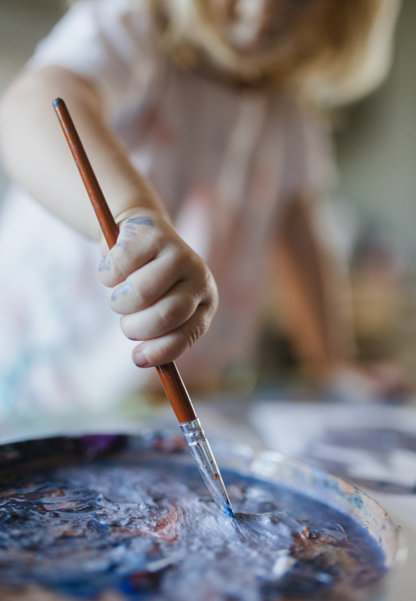 Close-up of child's hand holding paintbrush, painting with tempera paint. Dipping the brush in paint.